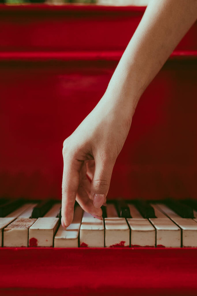 a close-up of a side view with female hand with pink manicure playing the piano. An old red piano with black and white keys. A palm above the keyboard. Graceful fingers of composer or musician - Fotografie, Obrázek