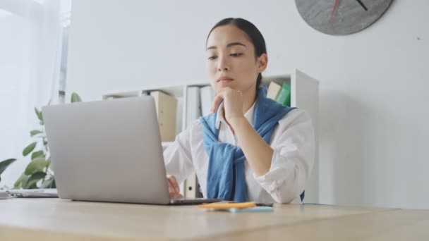 A focused thoughtful young asian secretary woman is using her laptop computer while working in an office - Video