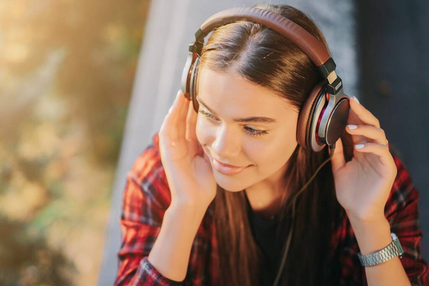 Słodka twarz dziewczyny ze słuchawkami. Młoda kobieta lubi muzykę siedząc w zielonym parku. Pojęcie młodości, wolności, technologii - Zdjęcie, obraz