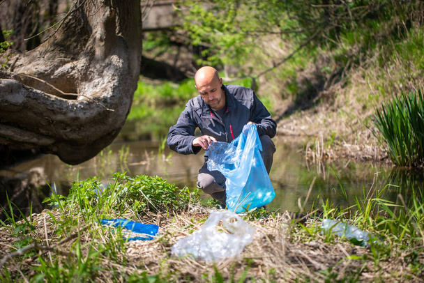 Mies poimien muovipullo, roskat kerätä metsän puhdistus planeetta, roskat kokoelma hyväntekeväisyyteen ympäristö
 - Valokuva, kuva