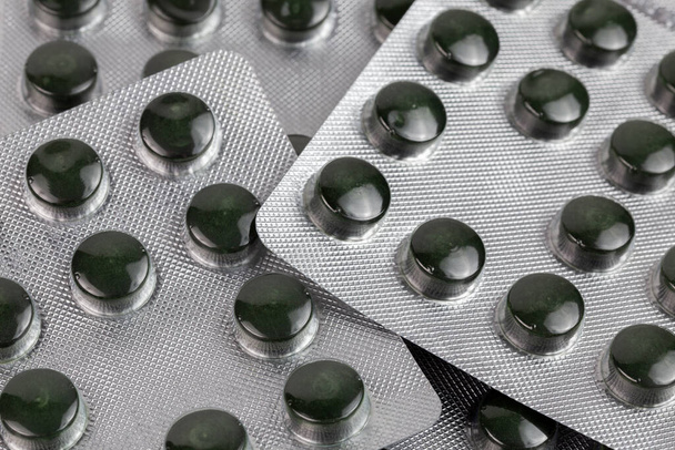 identieke groene spirulina pillen in medische blisterverpakkingen close-up met selectieve focus en achtergrond vervaging - Foto, afbeelding