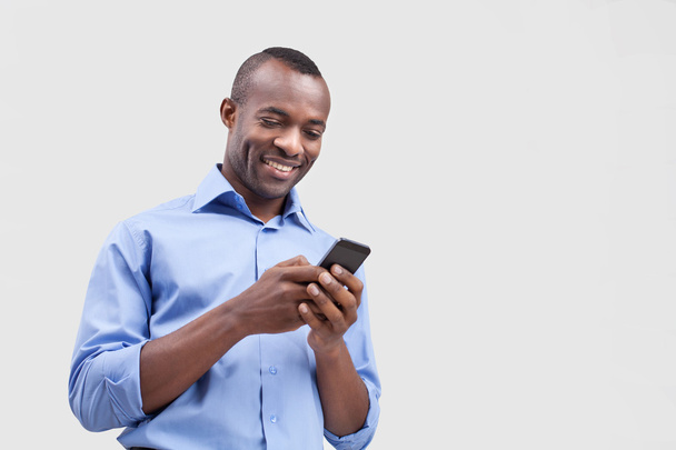 Hombre negro escribiendo algo en el teléfono móvil y sonriendo
 - Foto, Imagen