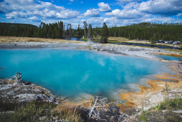 Becken mit blauem Farbton von thermischen Mikroorganismen im Inneren mit orangefarbener brauner Farbe an den Seiten im Yellowstone Nationalpark Vereinigte Staaten, Reisehintergrund mit Geysiren und heißen Quellen, berühmte Sehenswürdigkeiten. - Foto, Bild
