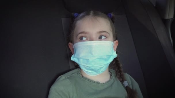 Menina triste em máscara protetora no banco de trás do carro em movimento no trânsito da cidade durante a epidemia de coronavírus e auto-isolamento
 - Filmagem, Vídeo
