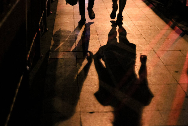 Σιλουέτες και σκιές των ανθρώπων στο φως της πόλης το βράδυ - Φωτογραφία, εικόνα