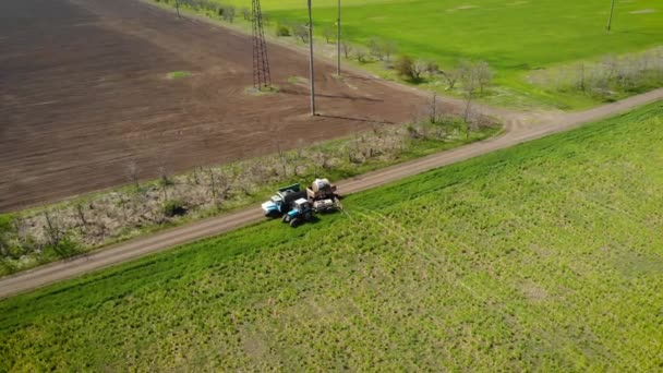 Luftaufnahme von Traktor mit Sprühgerät mit chemischen Herbiziden im Inneren und LKW mit Anhänger zwischen Feldern auf staubiger Straße - Filmmaterial, Video