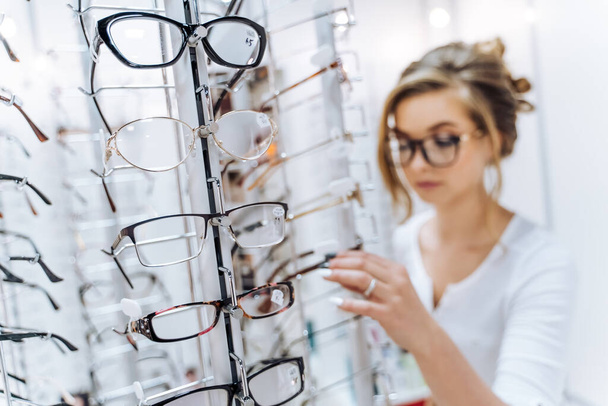 Stand of fashion elegance nglasses in the store. Showcase with glasses in modern ophthalmic store. Woman in the background. Closeup. - Fotografie, Obrázek