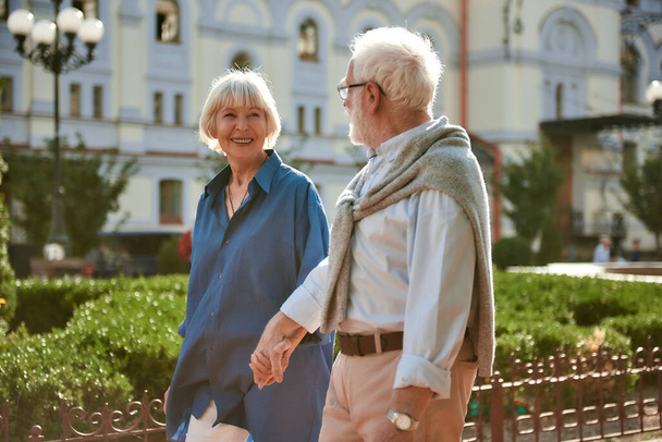 Ich liebe meinen Mann. Glückliches und schönes älteres Paar, das sich Händchen hält und einander beim Spazierengehen im Freien ansieht - Foto, Bild