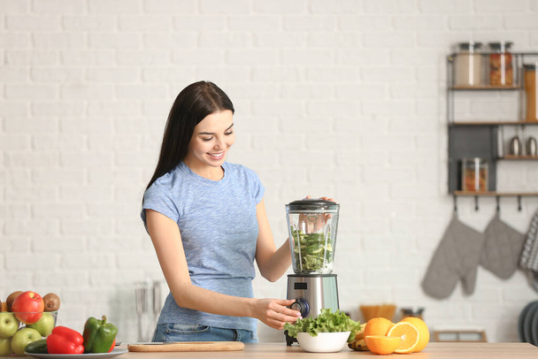 Jovem mulher fazendo smoothie vegetal na cozinha em casa
 - Foto, Imagem