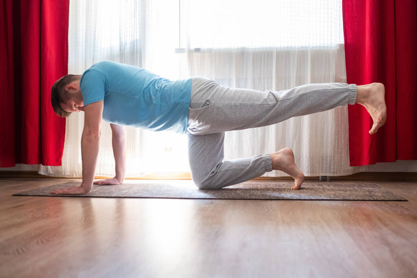 Joven hombre caucásico practica yoga asana chakravakasana o pájaro posan en la sala de estar en casa
. - Foto, Imagen
