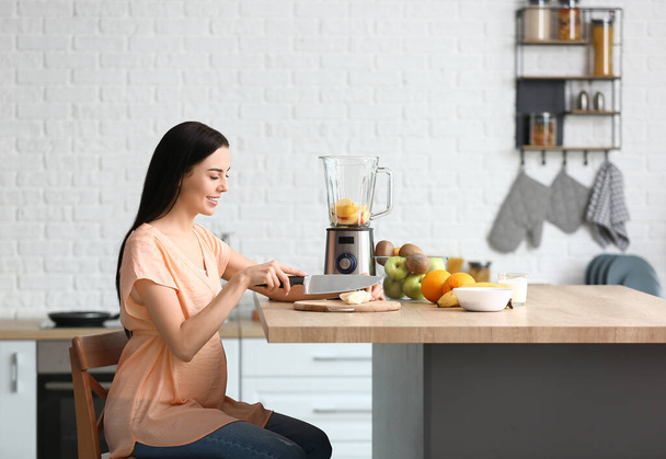 Mujer embarazada joven haciendo batido de frutas en la cocina en casa
 - Foto, imagen