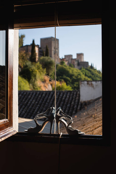Mavi gelinlik ayakkabıları silueti pencere çerçevesine yaslanmış, arka planda Alhambra manzaralı. - Fotoğraf, Görsel