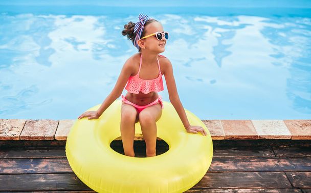 Cheerful girl sitting on swim tube on poolside - Foto, Imagen
