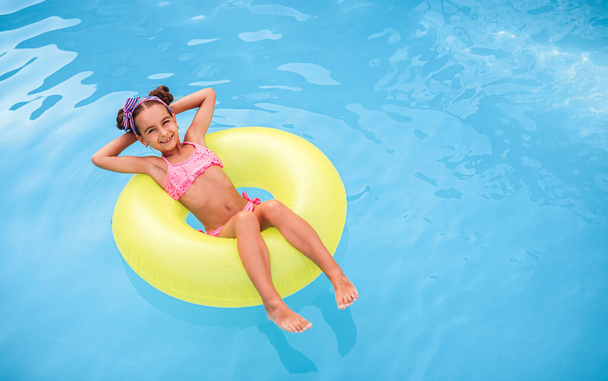 Happy girl floating on pool water - 写真・画像
