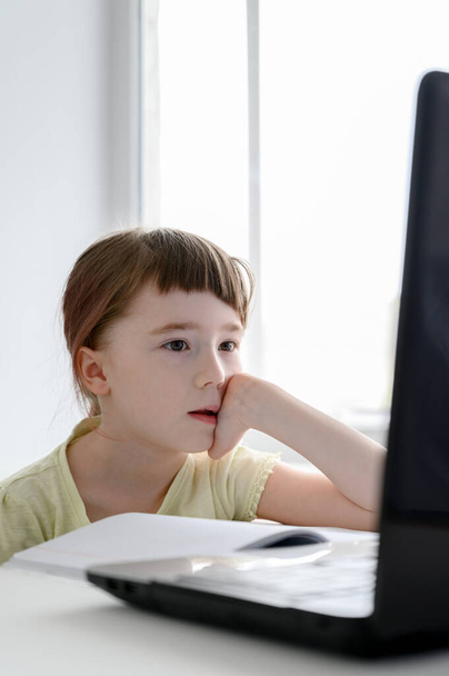 遠隔オンライン教育。10代の女子学生はノートパソコンを使って家で勉強している。白人の女の子はベッドに座って学校の宿題をする. - 写真・画像