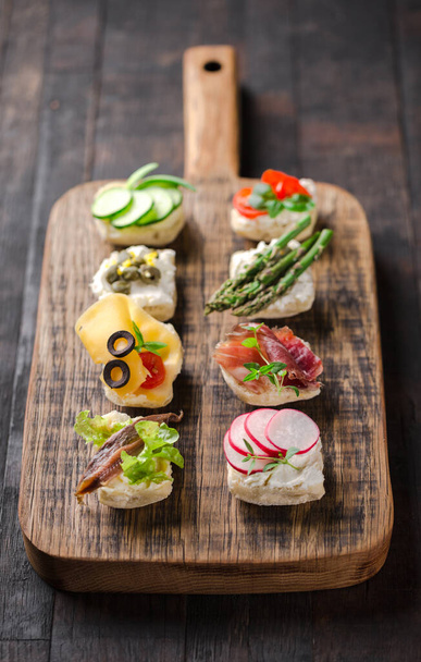 Catering set of different mini canapes served on a wooden board. - Fotó, kép