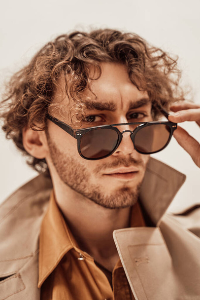 Handsome and casual-looking man posing for the photoshoot on the while background and taking his glasses off - Photo, Image
