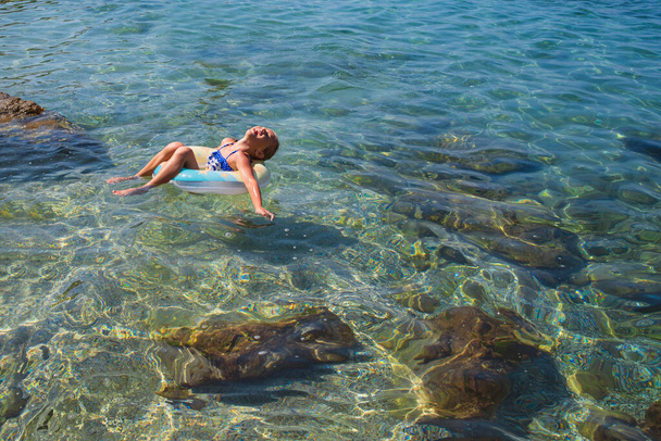 Kaunis tyttö rentouttava puhallettava kumi ympyrä meressä.Pieni tyttö ui ja meri puhallettava ympyrä. Tyttö puhallusympyrässä. Merimaisema
. - Valokuva, kuva
