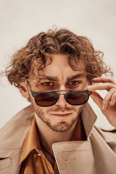 Porträt eines hübschen, lässigen Typen mit lockigem Haar, der im hellen Studio posiert und seine Brille abnimmt - Foto, Bild