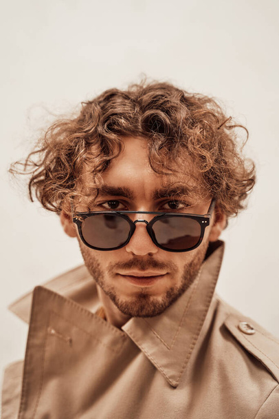 Cool and assertive young man with curly hair posing on the white background of the studio looking right on camera - Fotoğraf, Görsel