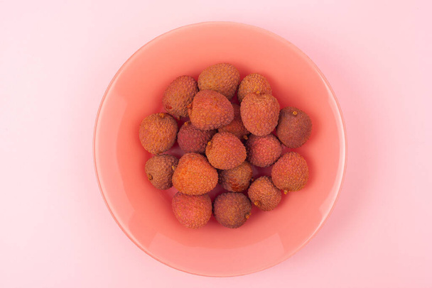 several lychee fruits lie on a coral plate on a pink background - Foto, immagini