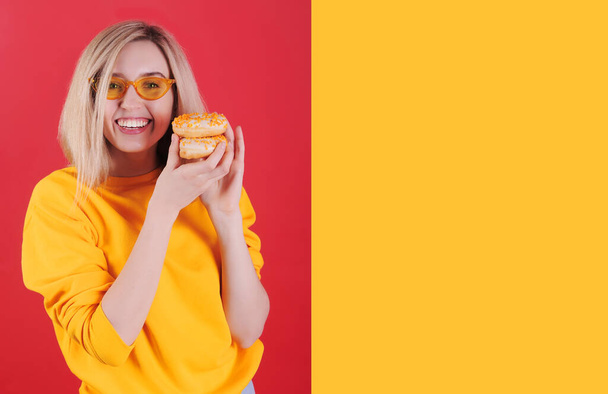 Femme caucasienne souriante en pull jaune avec des beignets jaunes posant sur fond rouge
. - Photo, image