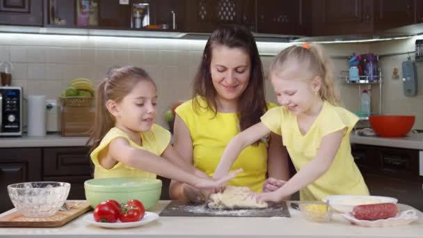 Mama und ihre beiden Töchter haben Spaß in der Küche. Mama bringt Kindern bei, wie man Pizza macht. Glückliche Mutter und glückliche Kinder kochen gemeinsam in der Küche. - Filmmaterial, Video