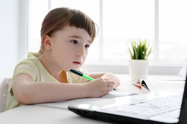 Kształcenie online na odległość. Uczennica uczy się w domu, używa laptopa. Biała dziewczyna siedzi przy stole i odrabia lekcje.. - Zdjęcie, obraz