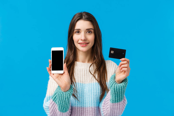 Waist-up portrait assertive young woman smiling, showing how banking system works, connect bank account with smartphone application, holding credit card and mobile, showing something on display - Fotoğraf, Görsel