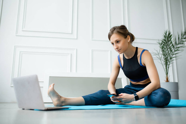 A woman watches sitting a fitness lesson at home on video tutorials on a laptop and holds a smartphone in her hands. - Foto, Imagen