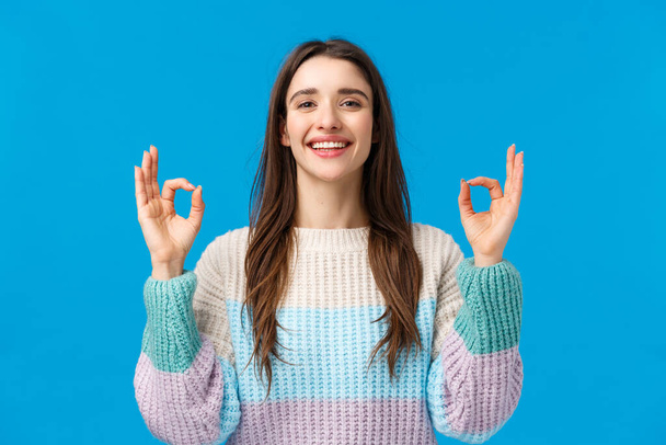Happy charismatic gorgeous woman in winter sweater, say yes, alright, showing okay gestures, rate excellent movie, perfect gift, spend awesome holidays on winter ski resort, blue background - Photo, Image