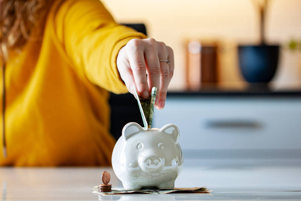 Personal finances, woman putting money into a piggy bank- -wealth and financial concept. White piggy bank in the foreground. - Фото, зображення