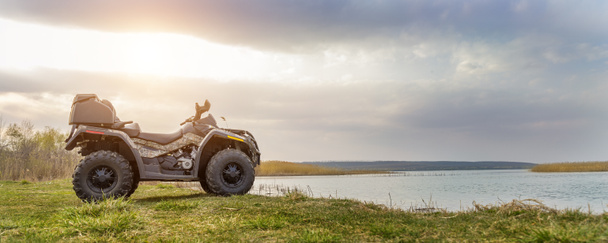 ATV awd quadbike motorcycle pov view near lake or river pond coast with beautiful nature landscape and cloudscape sky background. Offroad adventure trip . Extreme sport activity panoranic wide view - Photo, Image