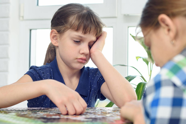 Tired girl reluctantly collects jigsaw puzzles with her friend - Foto, Bild