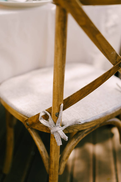 Eine Nahaufnahme der Rückenlehne eines Holzstuhls mit grauem Kissen, das mit einer Schleife an einen Stuhl gebunden ist. - Foto, Bild