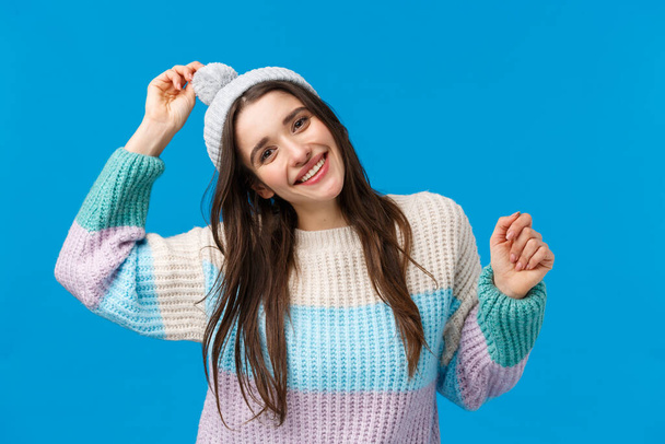Mujer joven bastante alegre y feliz, sonriente celebrar la Navidad, vacaciones de invierno, bailar y divertirse en la estación de esquí, montañas, usando sombrero y suéter, de pie feliz sobre fondo azul
 - Foto, Imagen