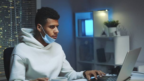 Plan moyen de bel homme multiracial buvant une tasse de café et travaillant sur ordinateur la nuit
 - Photo, image