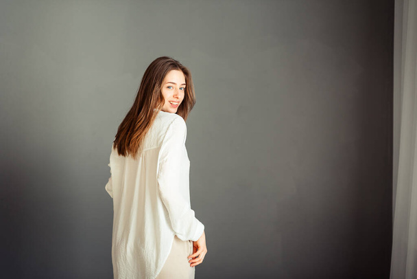 Fiatal lány fehér ingben, szürke háttérrel. Francia nő fehér blúzban, szürke falak mögött. Retusálás nélkül. - Fotó, kép