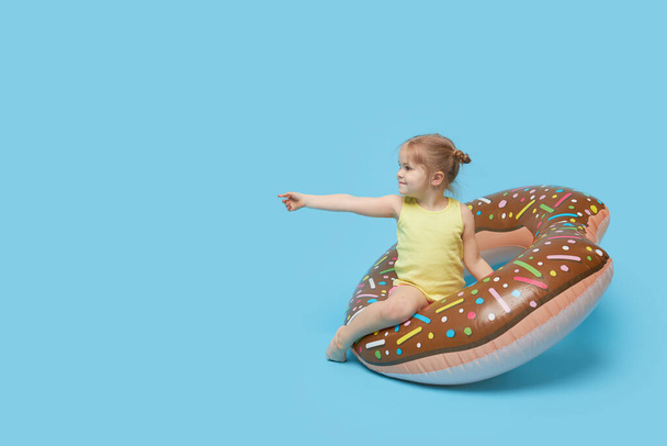 Failed summer vacation. Happy surprised child model girl resting on a donut-shaped rubber ring. Sea vacation concept on a colored blue background.  - Fotó, kép