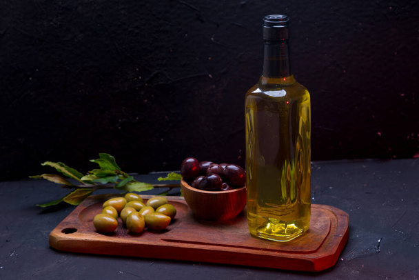 Flasche Olivenöl auf einem Tisch mit Oliven. - Foto, Bild