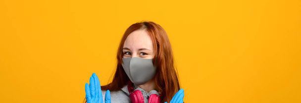 Портрет девушки в маске, которая надевает резиновую перчатку. Желтый фон. Изоляция, ковид-19
. - Фото, изображение