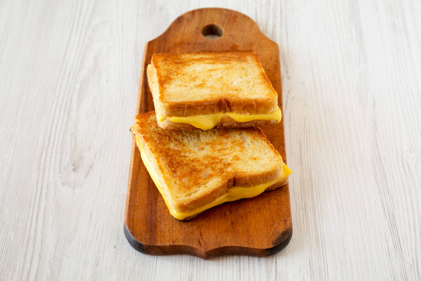 Σπιτικό σάντουιτς τυριού ψημένο σε ρουστίκ ξύλινη σανίδα σε λευκό ξύλινο φόντο, με χαμηλή γωνία θέας. Χώρος για κείμενο. - Φωτογραφία, εικόνα