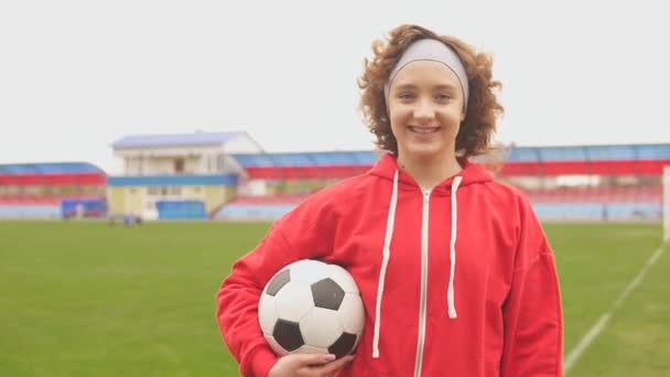 Portret van een lachende vrouwelijke voetballer met voetbal in het stadion - Video