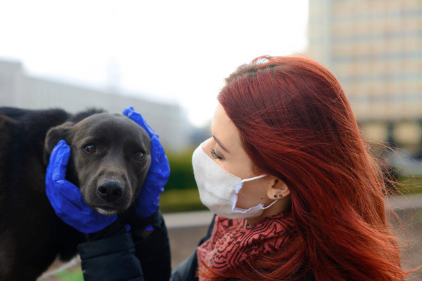 Νεαρό θηλυκό χρησιμοποιεί μια μάσκα προσώπου ως coronavirus εξάπλωση πρόληψη με τα πόδια με το σκύλο της. Παγκόσμια εικόνα έννοιας πανδημίας COVID-19. - Φωτογραφία, εικόνα