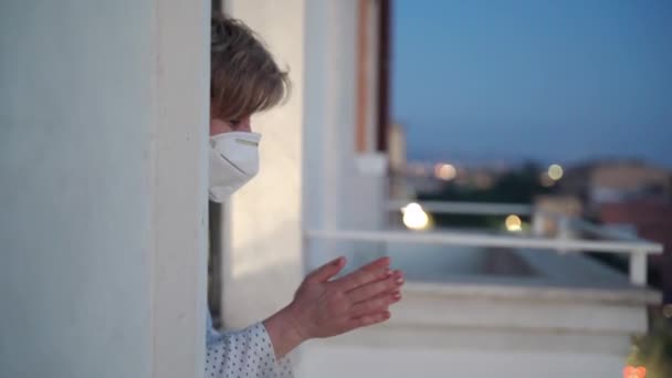 Mulher de meia-idade em quarentena com máscara protetora olhando pela janela e aplaudindo os profissionais de saúde que lutam contra o coronavírus na Itália. flash mob nacional em apoio de médicos e policiais
 - Filmagem, Vídeo