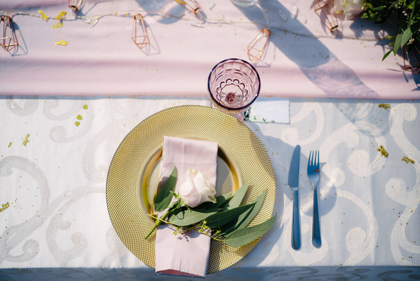 Ricevimento tavola nuziale. Piatto in oro con tovagliolo di stoffa rosa e foglie di ulivo. Lampone vetro vecchio. Una disposizione floreale al centro della tavola
. - Foto, immagini