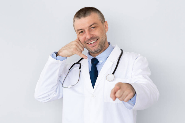 Portrait of mature doctor making call me gesture - Photo, image