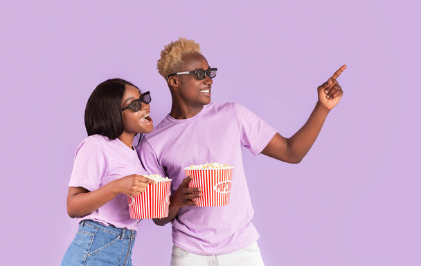 Kotiteatteri. Afrikkalainen amerikkalainen kaveri ja tyttö 3D-lasit ja popcorn poiminta elokuva katsella lila tausta
 - Valokuva, kuva