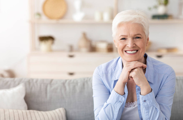 Έννοια Ασφαλούς Συνταξιοδότησης. Πορτραίτο της χαρούμενης ηλικιωμένης γυναίκας που ποζάρει στο σπίτι - Φωτογραφία, εικόνα