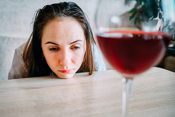 Eine Frau lehnt traurig mit dem Gesicht auf einem Tisch neben einem Glas Wein. Nahaufnahme. - Foto, Bild